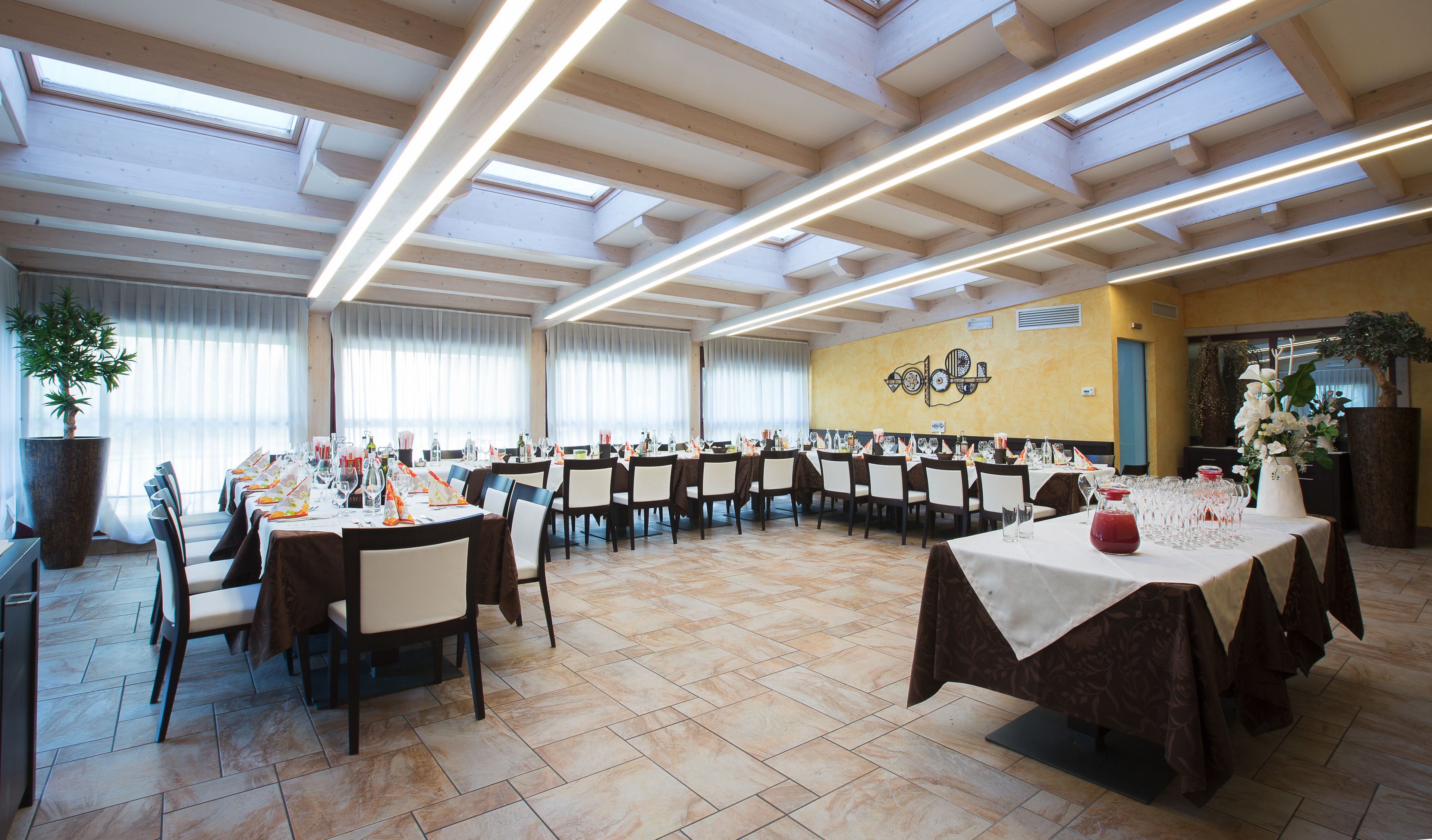 A banquet hall with multiple tables set for dining, large windows, and a decorative wall.