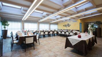 A banquet hall with multiple tables set for dining, large windows, and a decorative wall.