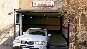 A white car parked at the entrance of a building labeled "Hotel - Ristorante PARCHEGGIO 1." - Hotel Ristorante Alla Nave (Lavis)
