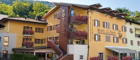 A hotel with a prominent staircase, balconies with flower boxes, and a sign indicating a restaurant.