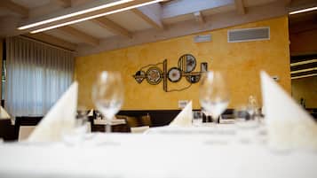 A restaurant interior with wooden beams, a yellow wall with a decorative metal piece, and tables set with glasses and napkins.