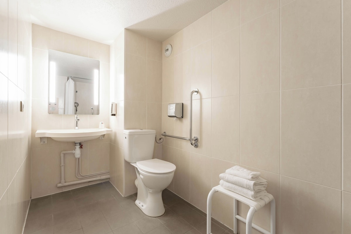 A modern bathroom with a toilet, sink, and handrails.