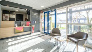 A reception area with a desk, chairs, and a large window. - B&B HOTEL Calais Coquelles Tunnel sous la Manche (Coquelles)