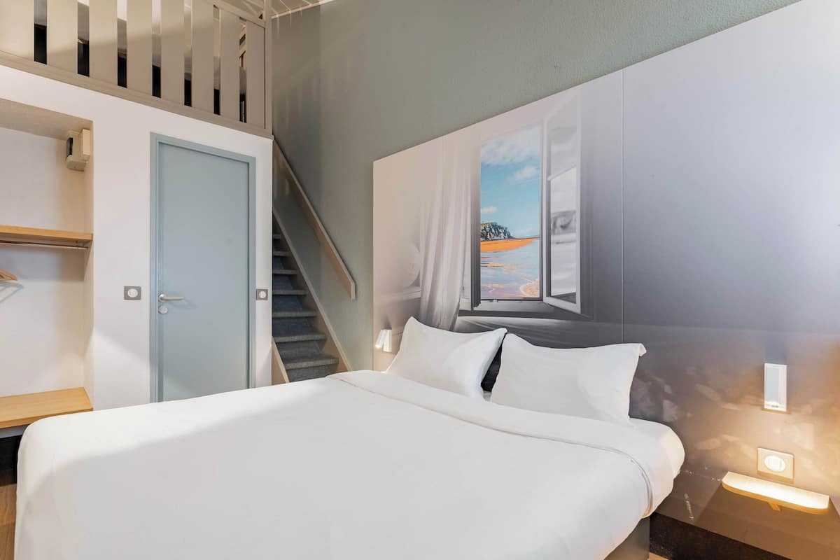 A hotel room with a bed, a desk, a wardrobe, and a staircase.