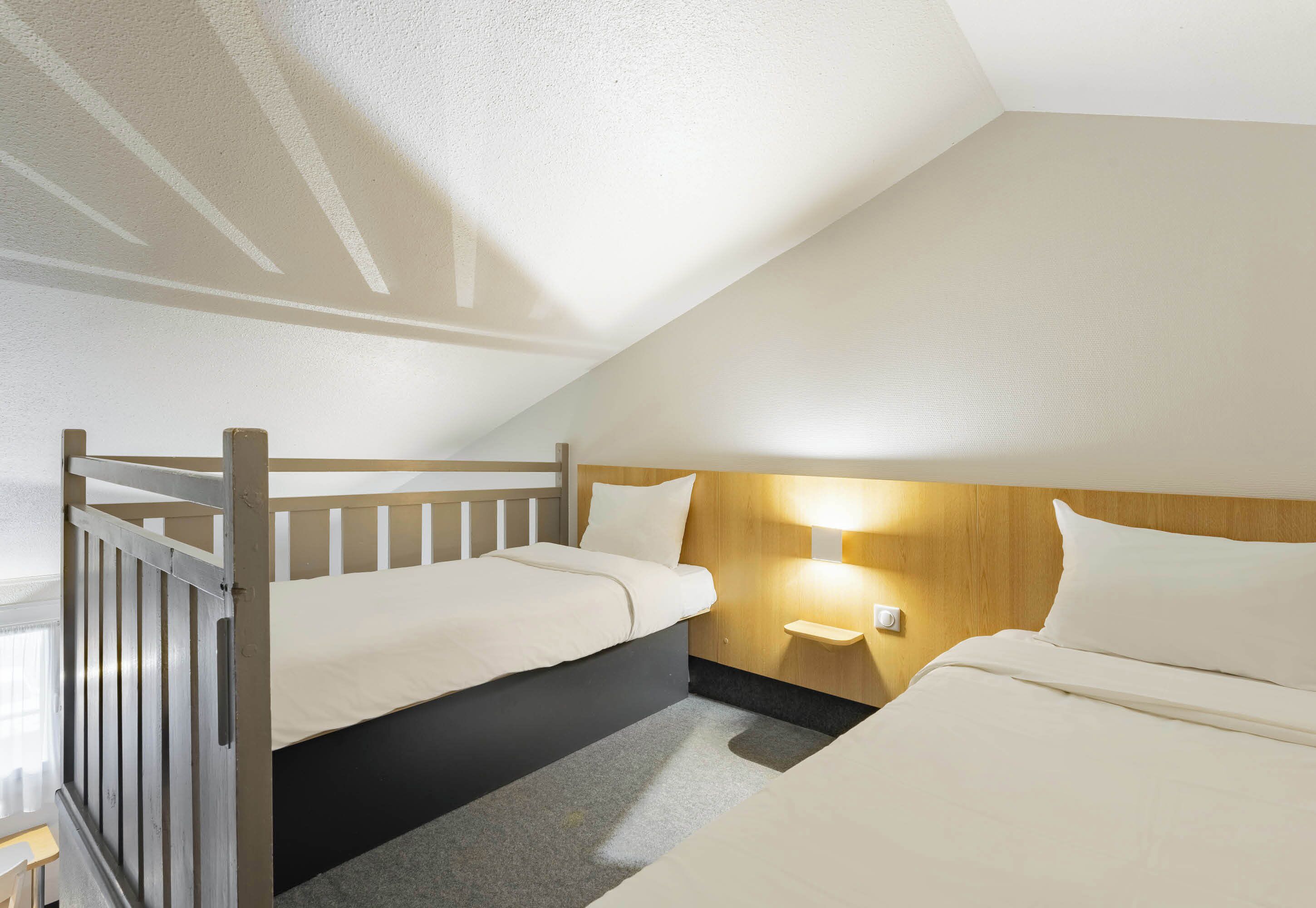 Una habitación pequeña y acogedora con una litera, una mesita de noche con lámpara y una ventana con cortinas.