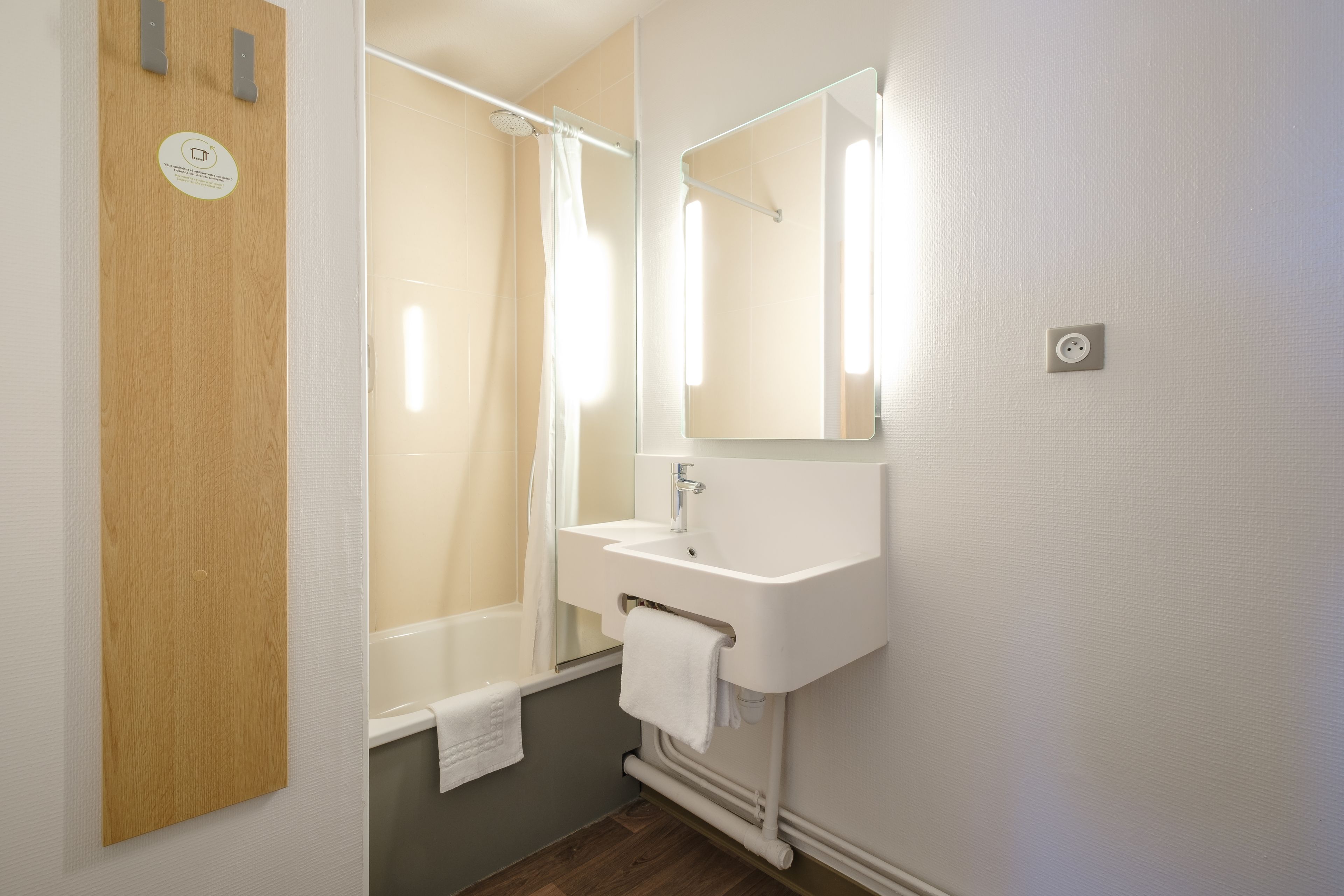 A bathroom with a wooden door, a white sink, a mirror, and a shower curtain.