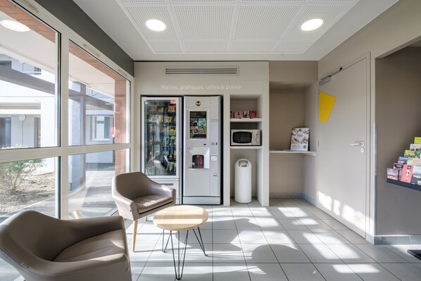 A modern interior with a seating area, a refrigerator, a microwave, and a trash bin.