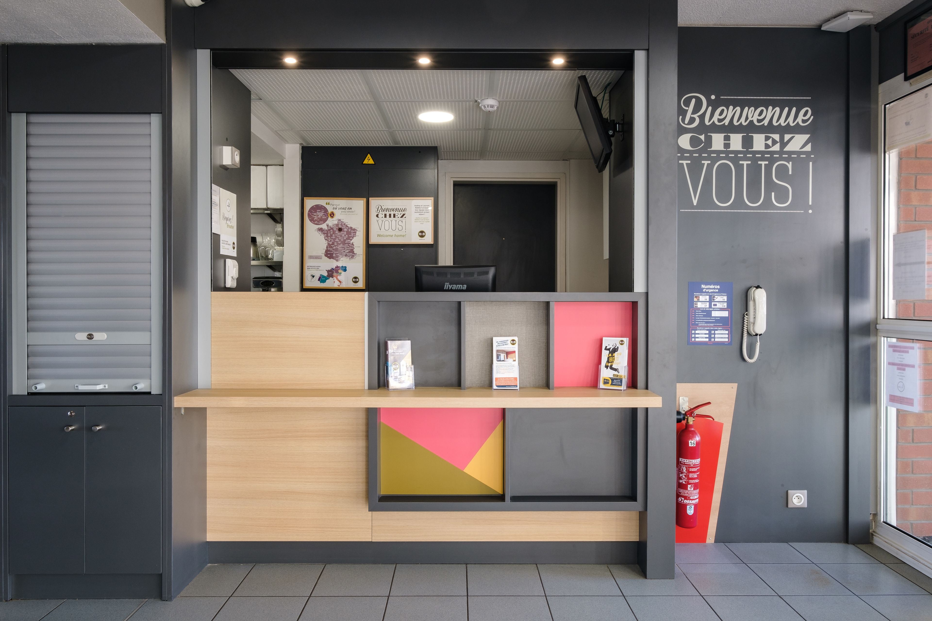 Un comptoir d’accueil au design moderne, un extincteur et une pancarte de bienvenue.