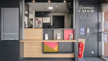 Un comptoir d’accueil au design moderne, un extincteur et une pancarte de bienvenue.