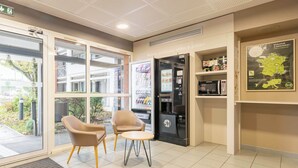 A hotel lobby with a seating area, a refrigerator vending machine, and a map on the wall. - B&B HOTEL Calais Coquelles Tunnel sous la Manche (Coquelles)