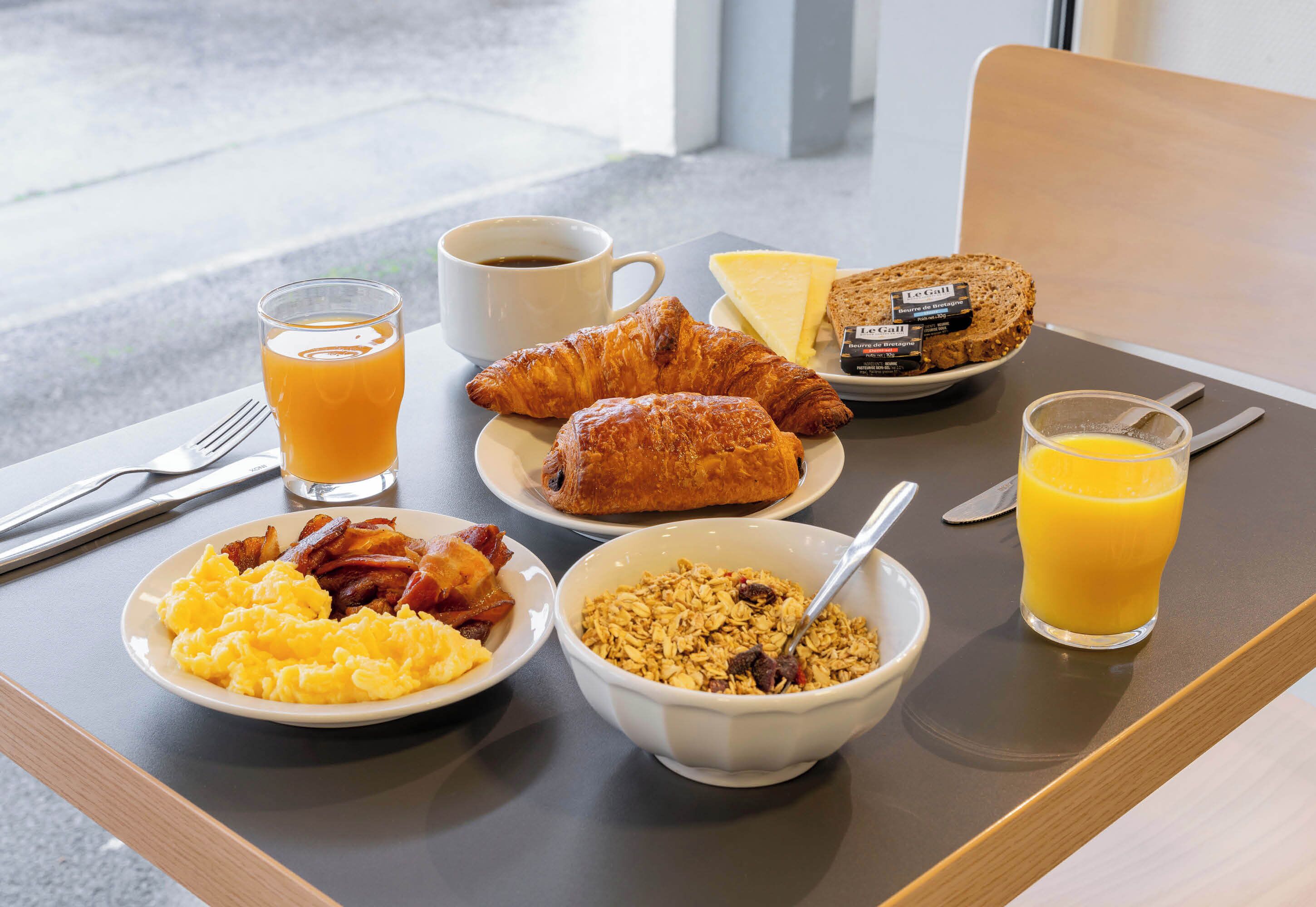 Een ontbijfwagen met croissants, roerei, spek, ontbijtgranen, sap en een koffiekop.