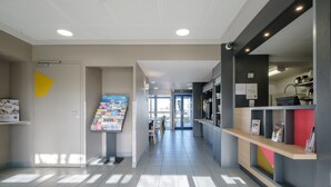 A modern hotel corridor with a reception desk, a bulletin board, and a seating area. - B&B HOTEL Calais Coquelles Tunnel sous la Manche (Coquelles)