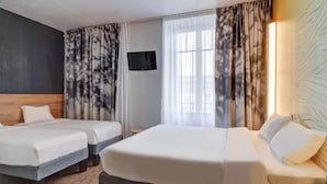 Una habitación de hotel con dos camas, televisión y un ventanal grande con cortinas.