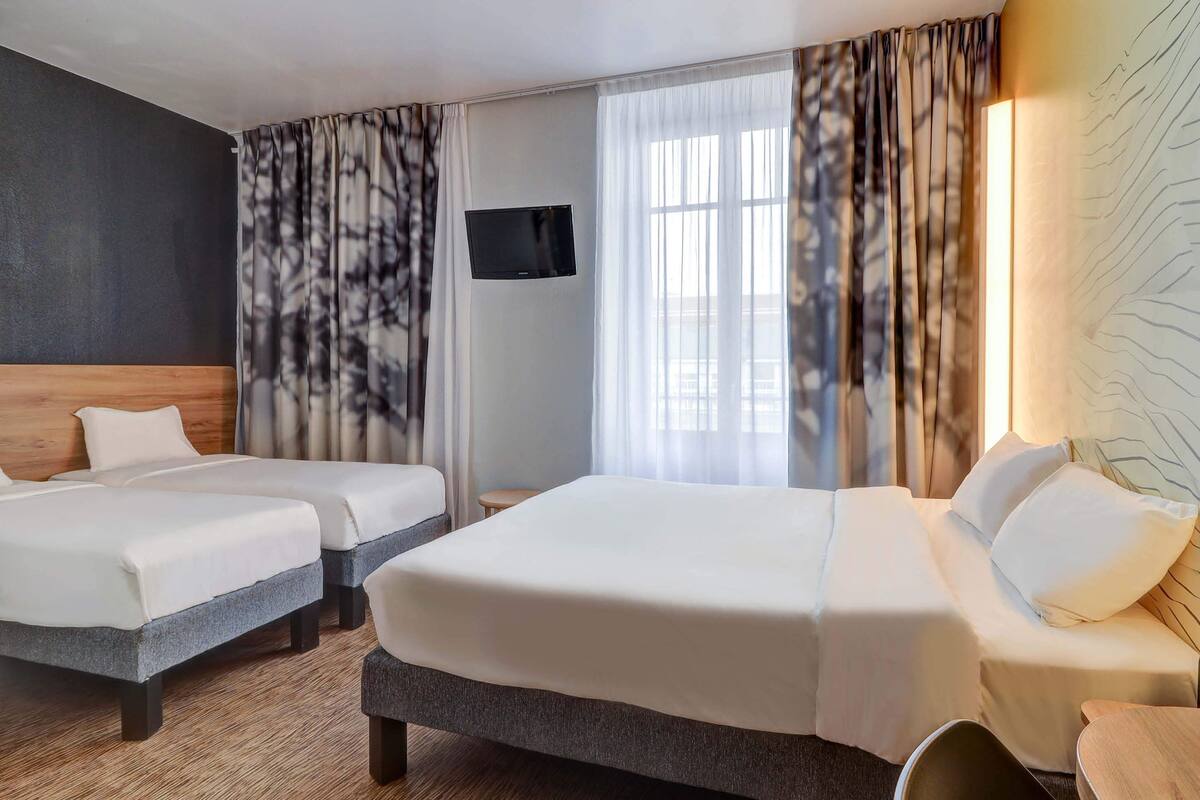 A hotel room with two beds, a TV, and a large window with curtains.