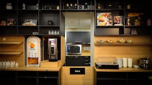 Una kitchenette con cafetera, microondas y diversos alimentos en estantes.