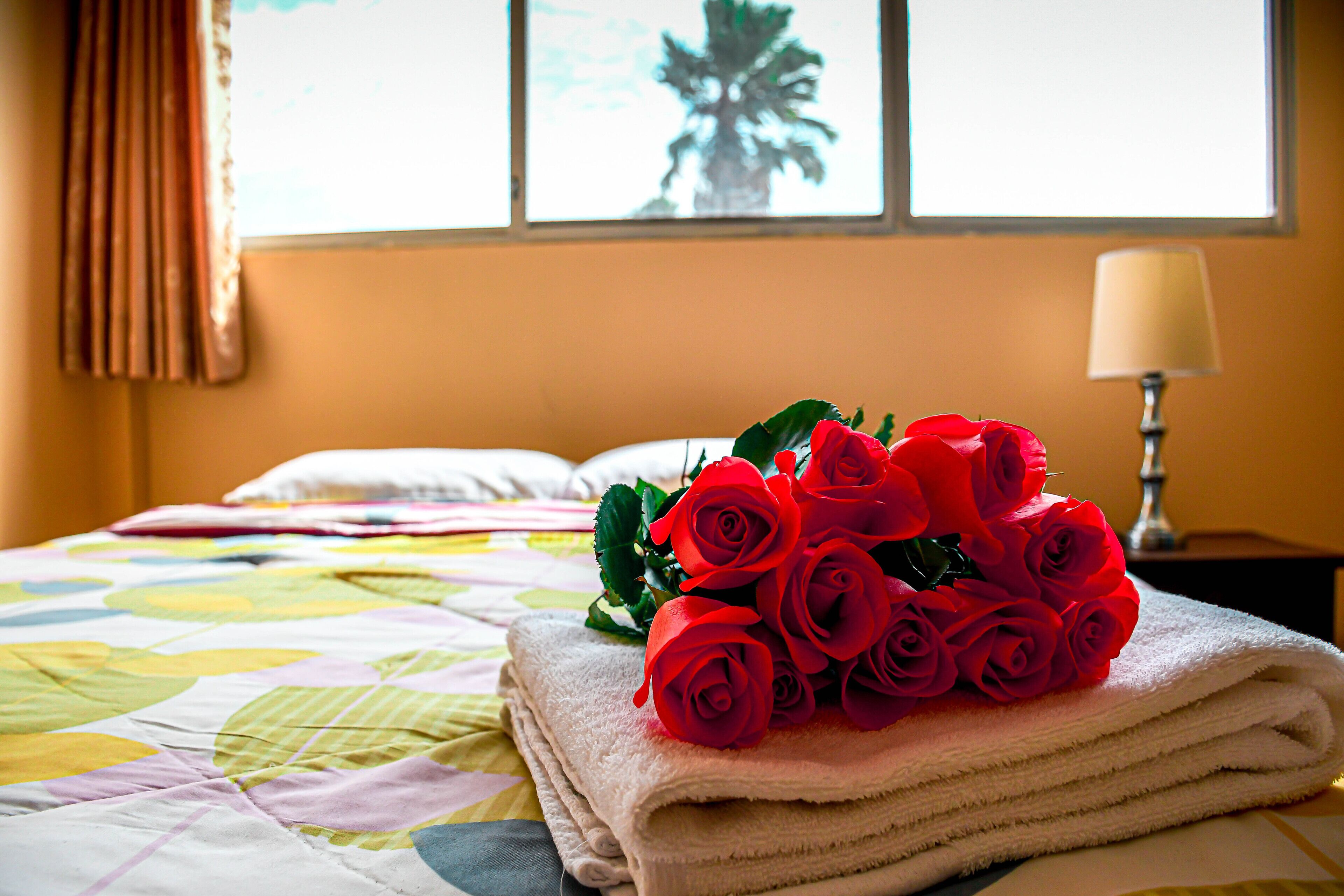 Una cama bien hecha con un edredón colorido, una pila de toallas blancas y un ramo de rosas rojas encima.