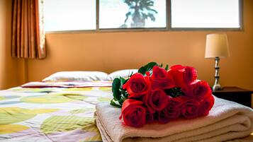 Una cama bien hecha con un edredón colorido, una pila de toallas blancas y un ramo de rosas rojas encima.
