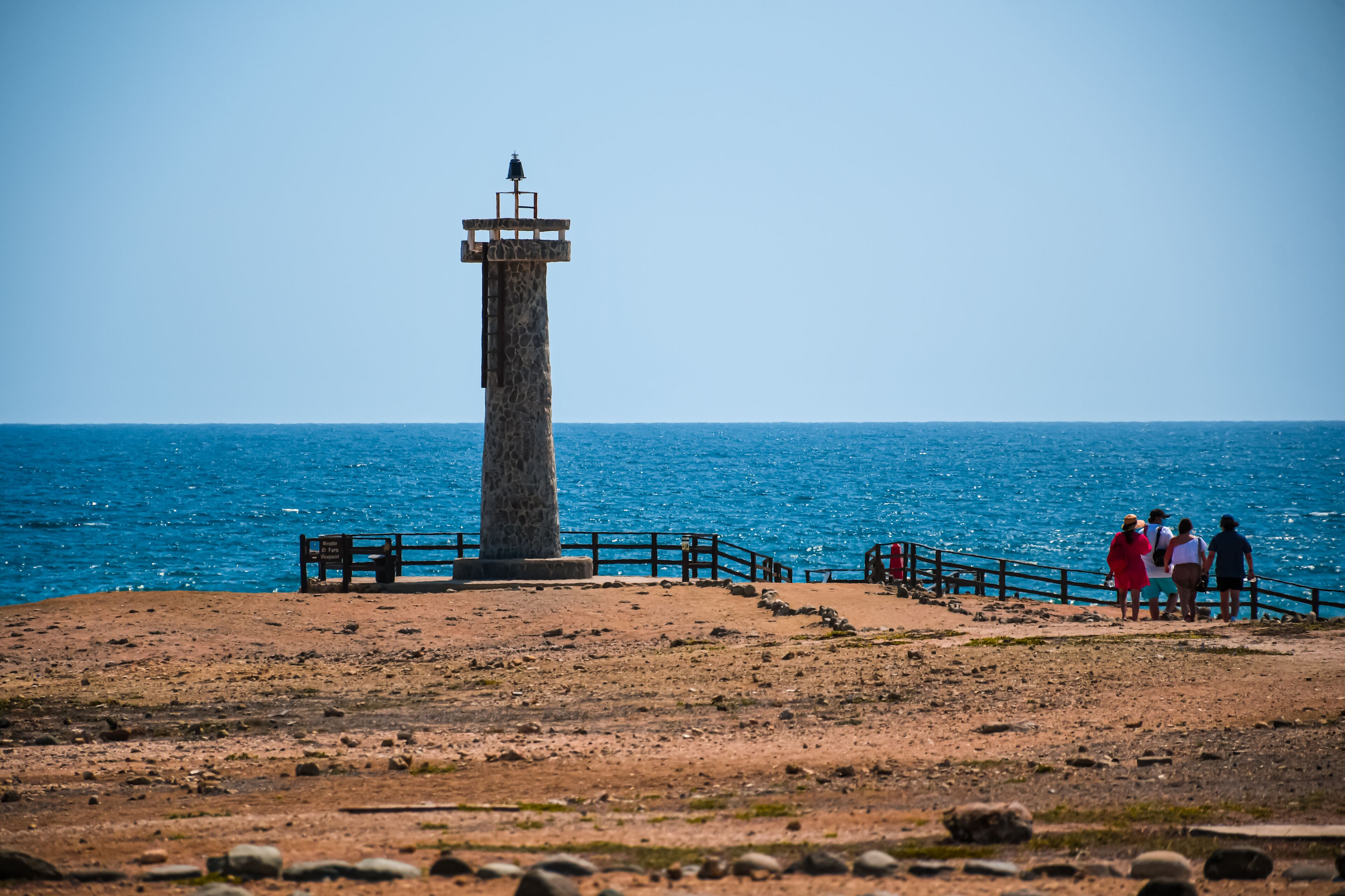 A coastal lighthouse with a clear view of the sea, a wooden bench, and a railing.