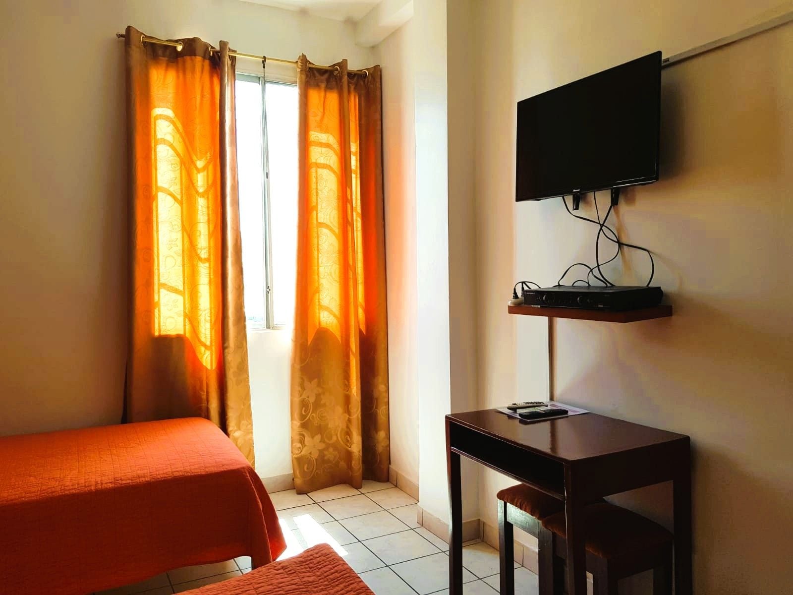 Ein Zimmer mit einem Bett, einem Schreibtisch, einem Fernseher und Vorhängen.