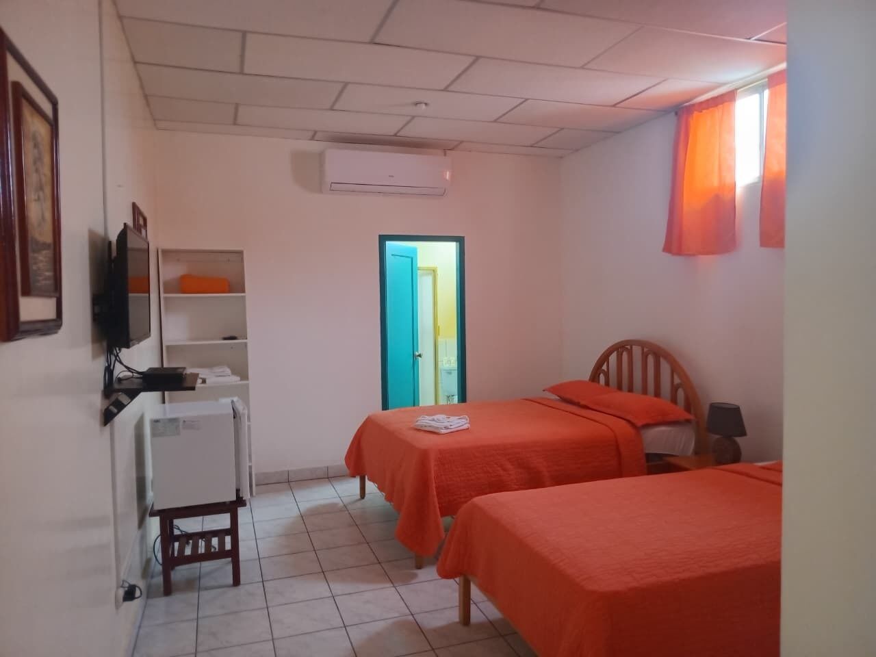 Habitación con dos camas, un escritorio, una silla, un televisor y una puerta que da a otra habitación.