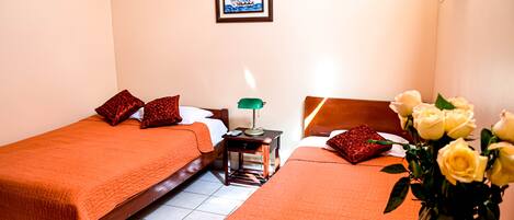 A hotel room with two beds, a nightstand, a lamp, a framed picture on the wall, and a vase with flowers.