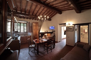 Una cocina rústica con vigas de madera, un comedor con mesa y sillas, y una sala de estar con sofá.