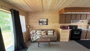 Interior acollidor d'una cabana amb sostre de fusta, un sofà amb coixinets estampats, una taula petita i una zona de cuina amb electrodomèstics.