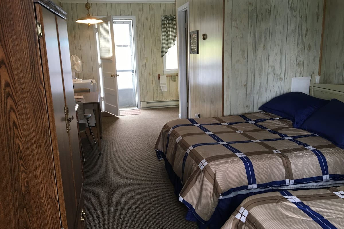 A bedroom with a bed, a desk, and a door leading to another room.