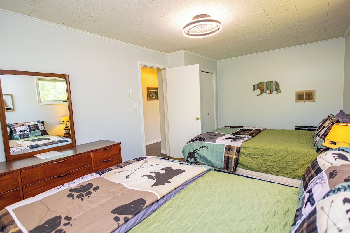 A bedroom with two beds, a dresser, a mirror, and a door leading to another room.