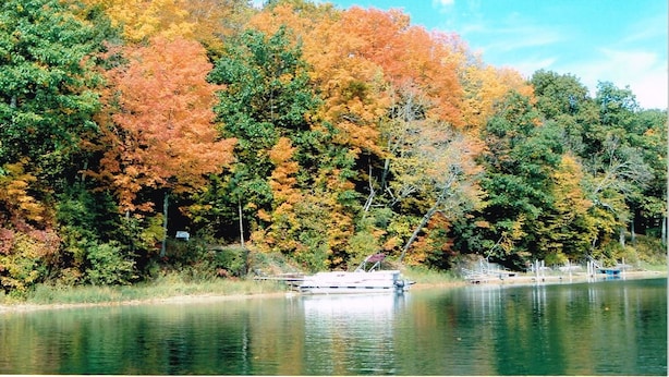 Un llac amb una barca amarrada a la riba, envoltat d'arbres de tons autunnals.