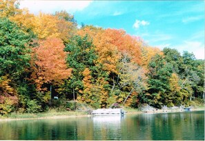 A lake with a boat docked on the shore, surrounded by trees in autumn colors. - Dixon Lake Resort (Gaylord)