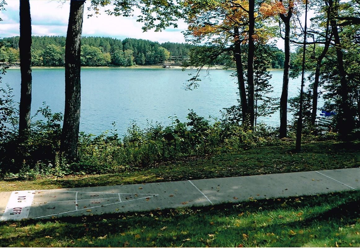 A lakeside view with a concrete path leading to the water, surrounded by trees and greenery.