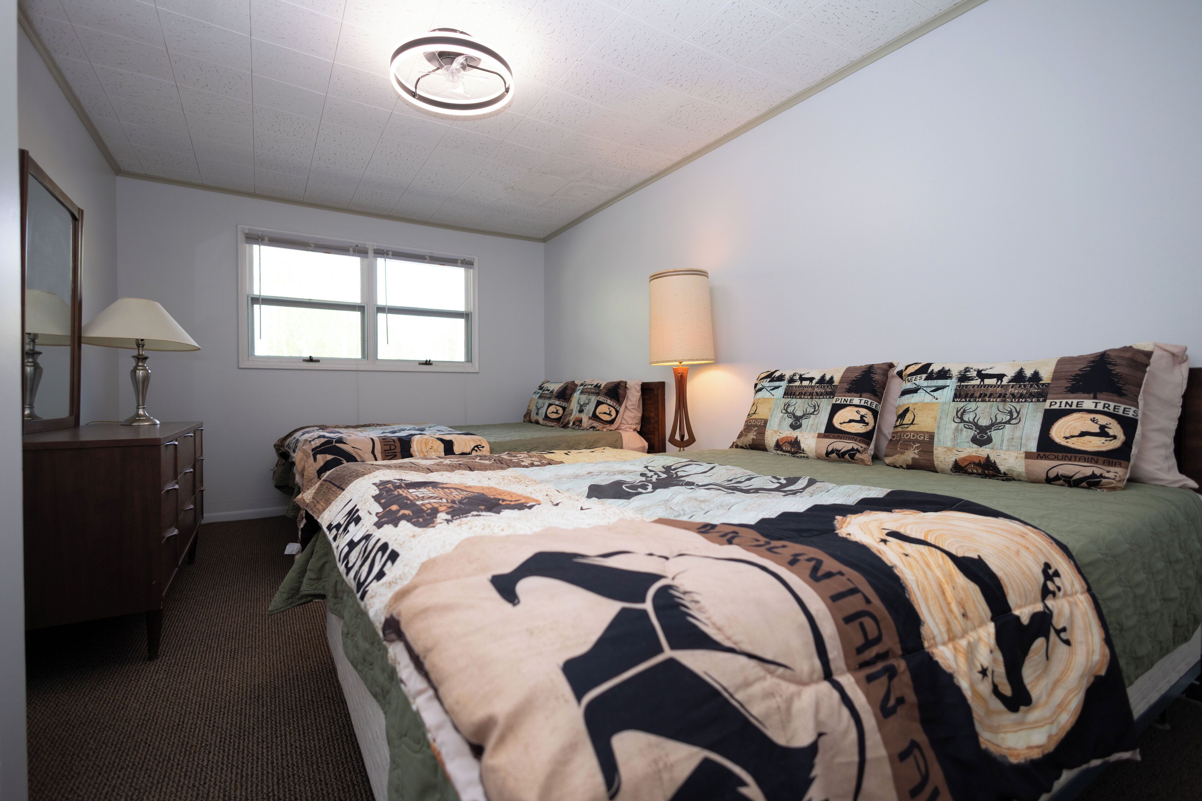 A bedroom with a bed, a dresser, a lamp, and a window.