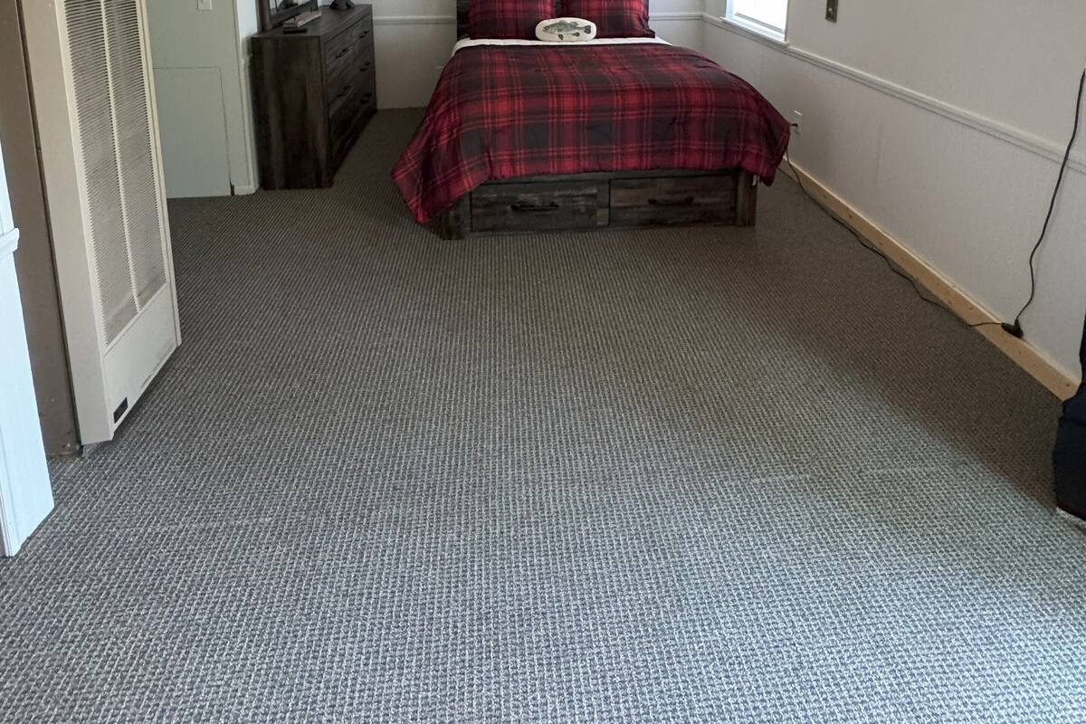 A bedroom with a wooden ceiling, a bed with a red plaid bedspread, a dresser, a mirror, and a television on the wall.