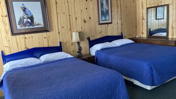 A room with two beds, wooden walls, a framed picture, a lamp, and a mirror.