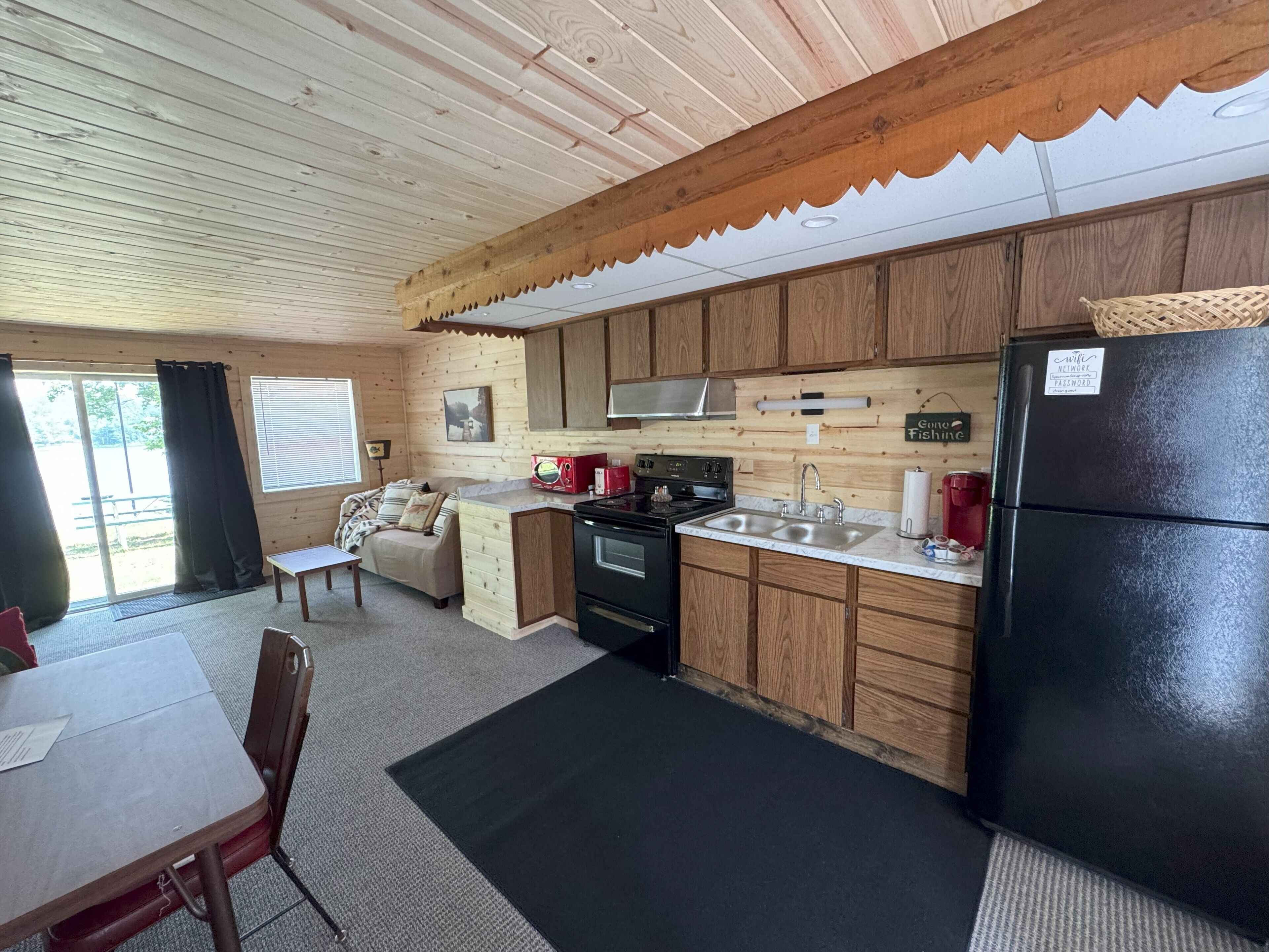 A cabin-style kitchen with wooden cabinets, a black refrigerator, a stove, and a sink.