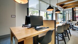 A modern workspace with a wooden desk, computer, and black chairs. - Hyatt House Chicago/Evanston (Evanston)