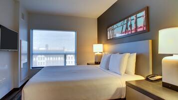 Habitación de hotel con una cama grande, televisión, ventana con vistas, un cuadro en la pared y una lámpara de noche.