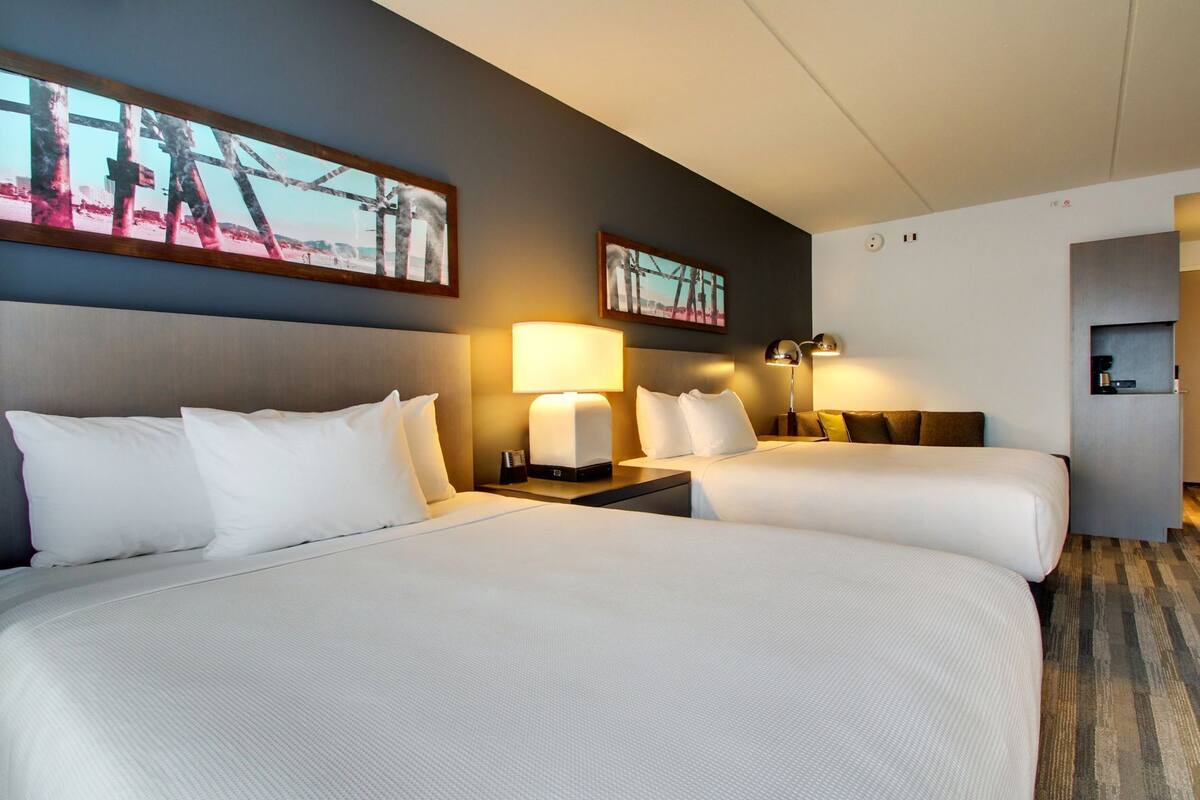 A hotel room with two beds, a nightstand with a lamp, and a painting on the wall.