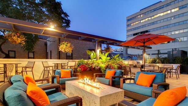 An outdoor seating area with wicker furniture, a fire feature, and a large umbrella. - Hyatt House Chicago/Evanston (Evanston)
