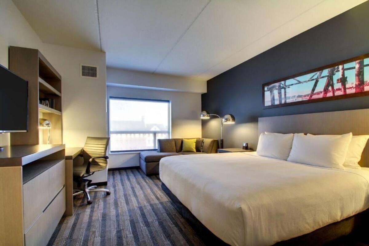 A hotel room with a large bed, a desk with a chair, a window, and a painting on the wall.