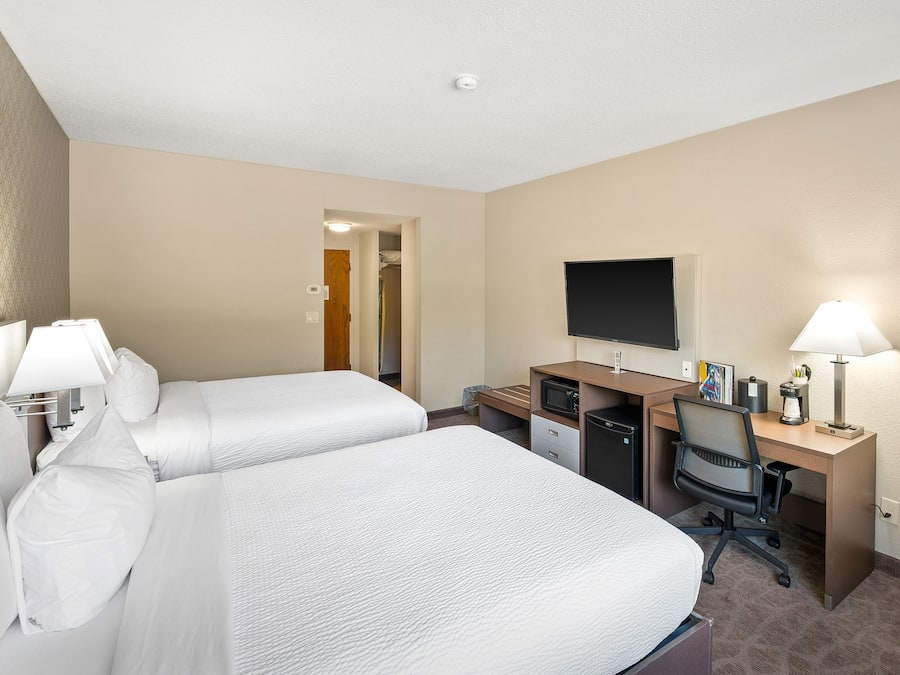 Habitación de hotel con dos camas, un escritorio, una silla, un televisor de pantalla plana y una lámpara.