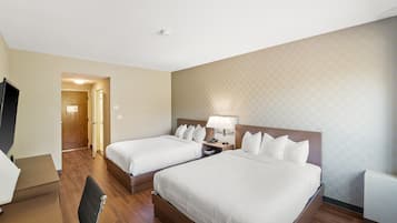 A hotel room with two beds, a desk, a chair, a TV, and a patterned wall.