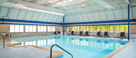 An indoor swimming pool with clear blue water, a metal ladder, and several lounge chairs along the poolside.