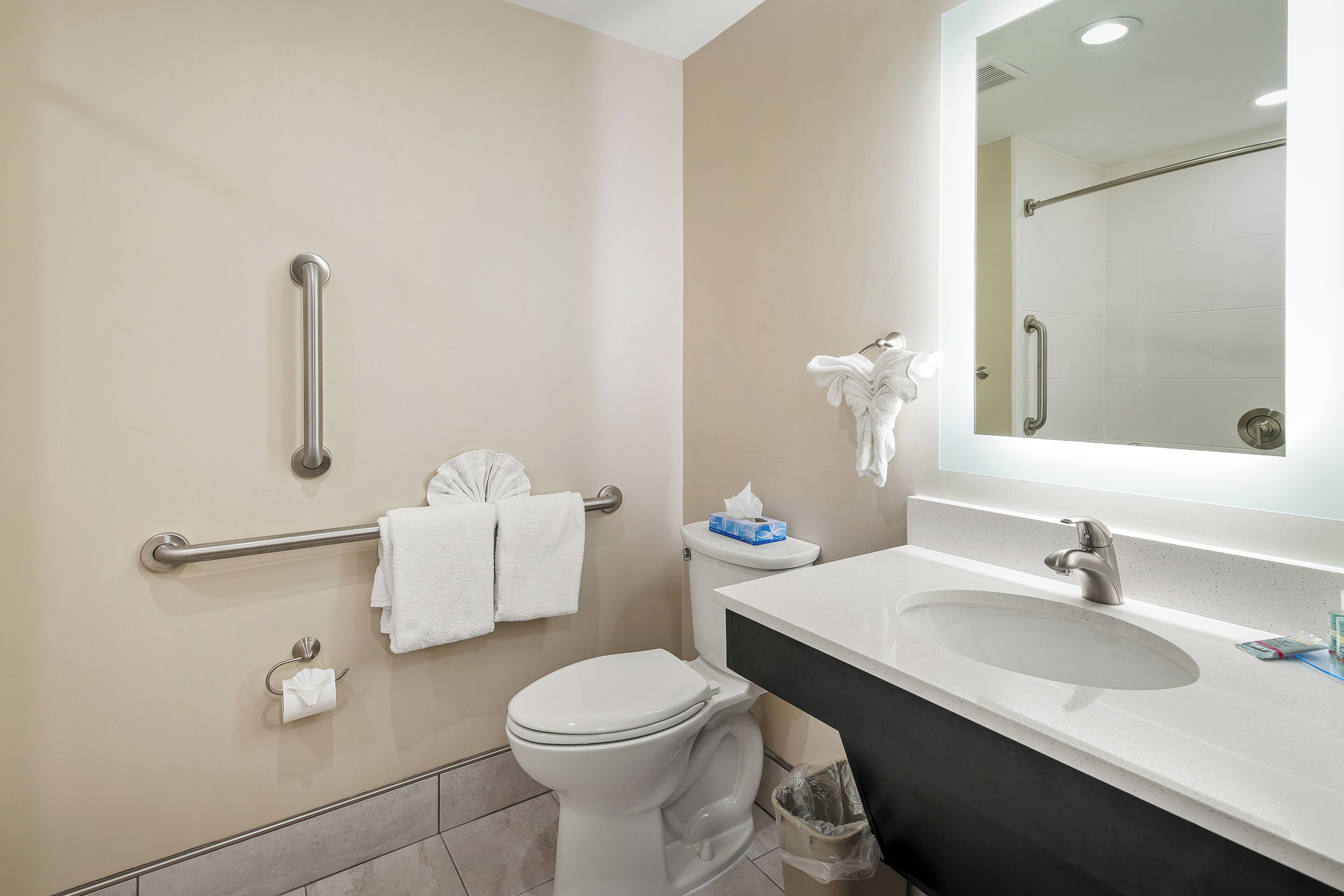 A modern bathroom with a white toilet, a sink with a mirror above it, and a handrail on the wall.
