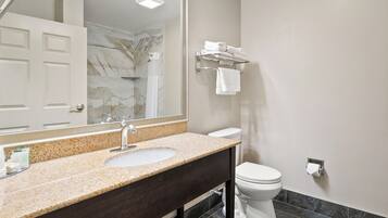 A bathroom with a granite countertop sink, a mirror, a towel rack, and a toilet.