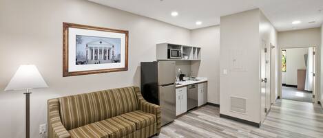 A modern hotel room with a striped sofa, a dining table, a kitchen area with a microwave, and a framed picture on the wall.