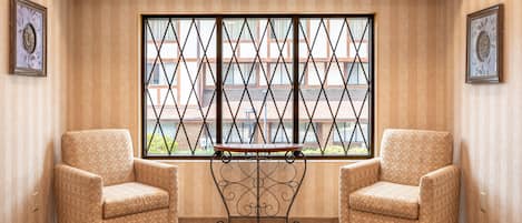A corner room with two armchairs, a patterned rug, and a window with a metal grille.