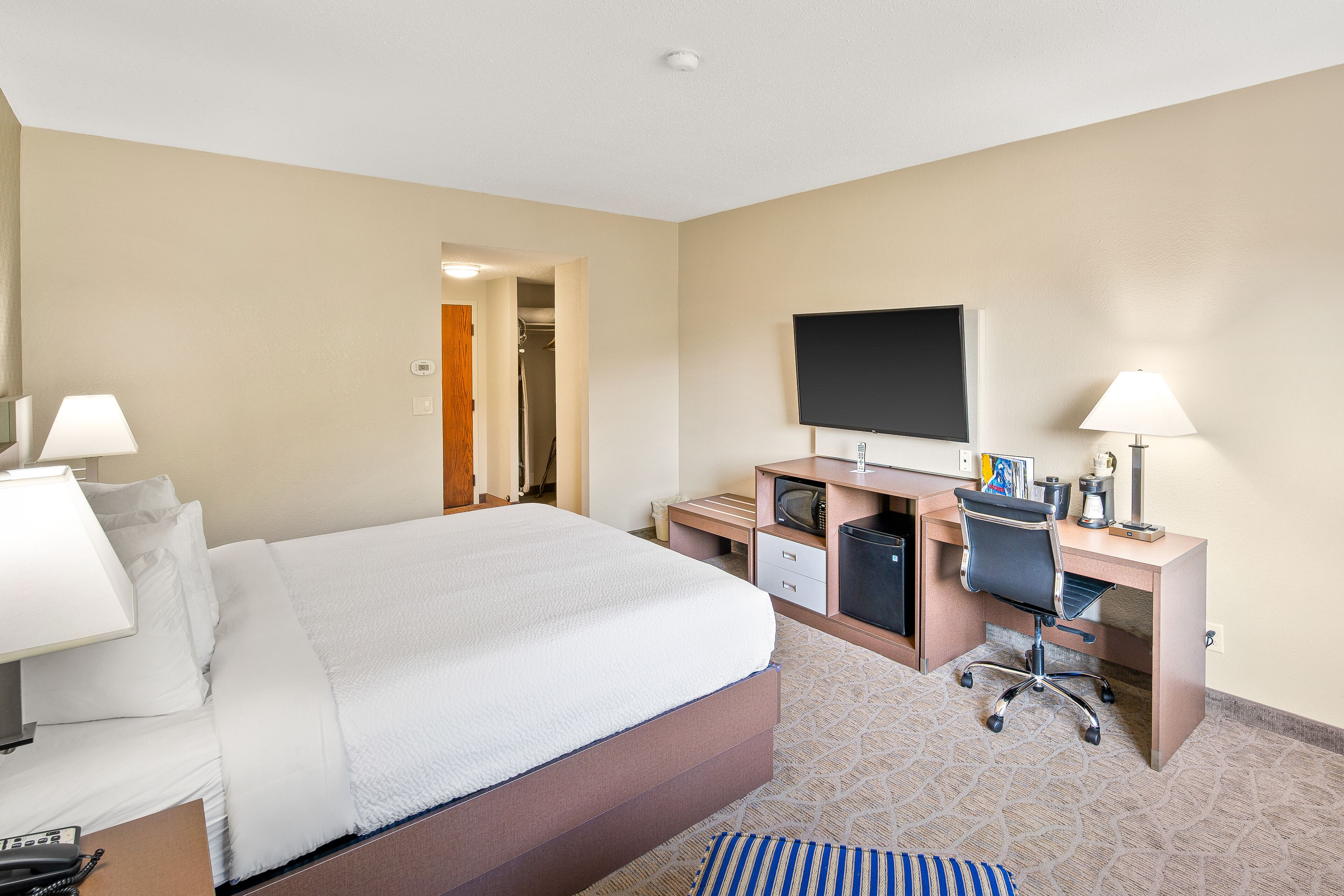 Ein Hotelzimmer mit Bett, Schreibtisch, Stuhl, Fernseher und einer kleinen Küchenzeile.