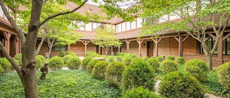 A courtyard with a brick building, surrounded by well-maintained hedges and trees.